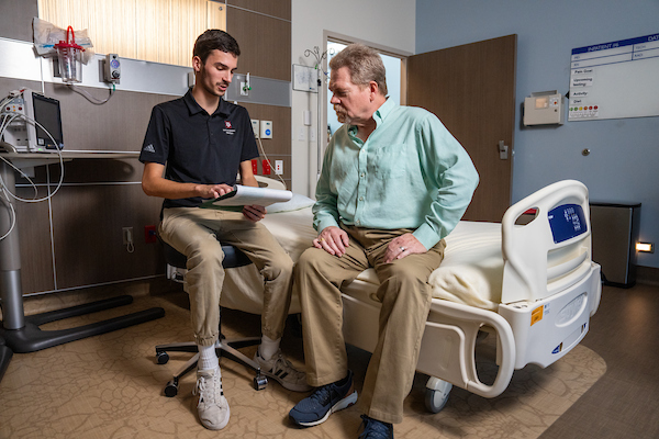 A nutrition student consults with a male patient in a hospital room