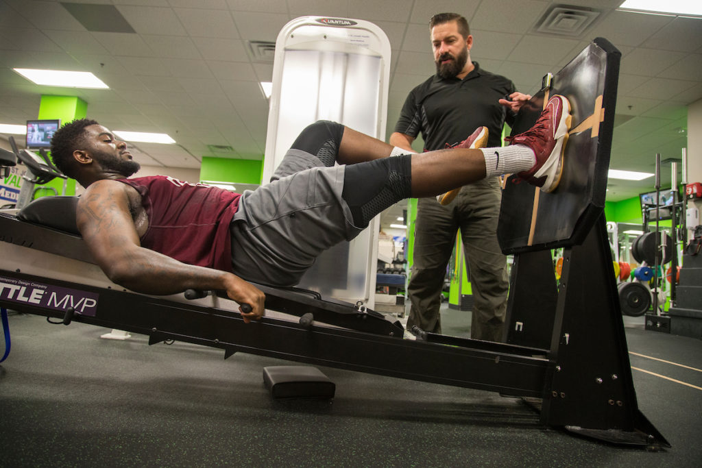 Man exercising using equipment in gym while another man talks