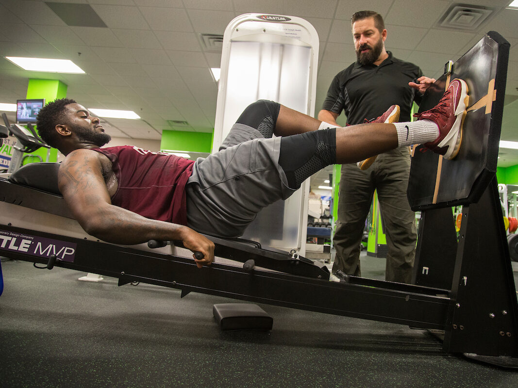 Man exercising using equipment in gym while another man talks
