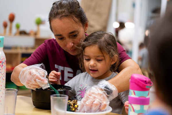 a student assisting a child with her meal at a childcare center