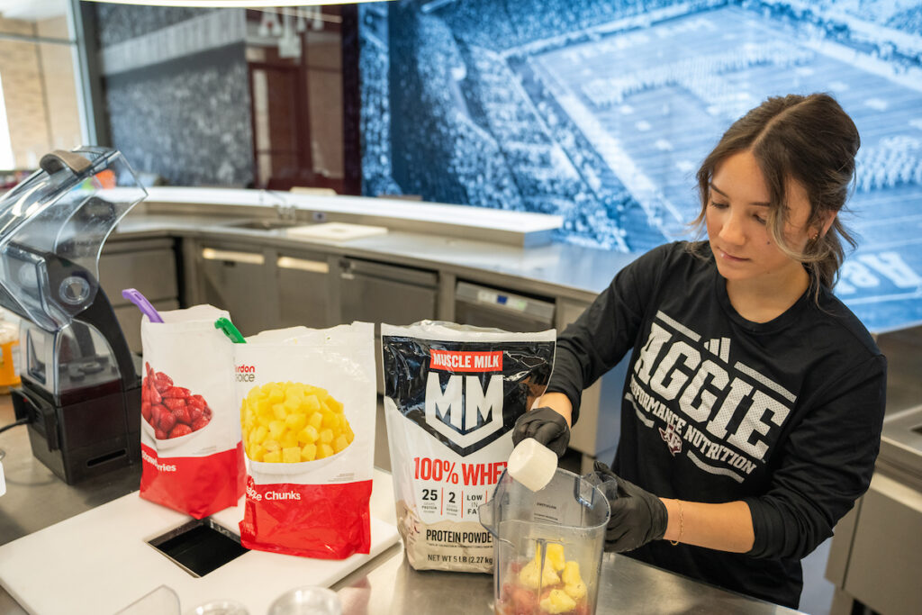 Woman scooping protein powder into a blender in front of a large image of Kyle Field